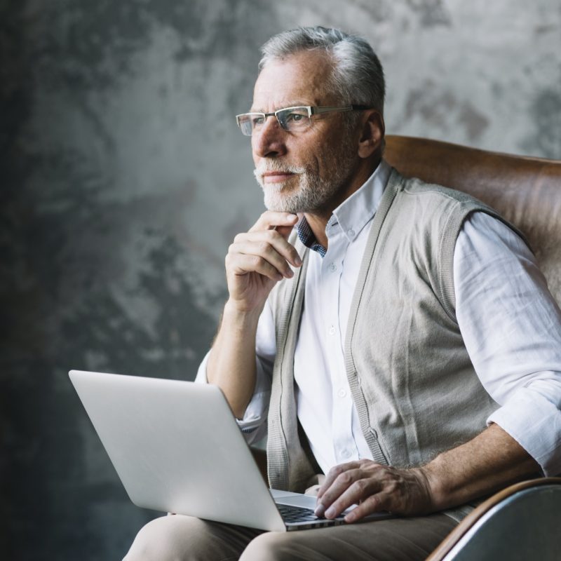contemplated-elderly-man-sitting-chair-with-laptop-against-grunge-background